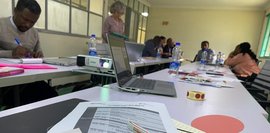 Foto des Feinplanungsworkshops am Selam College 2024. Tische mit Laptops, Projektor, Notizen und Personen in Diskussion. Materialien von Selam Children's Village und Partnerorganisationen liegen auf dem Tisch.