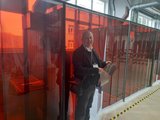 Ein Mann steht in Werkstatt und hält roten Schweißvorhang; weitere Streifen trennen Arbeitsbereich.