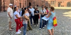 Stadtführung in Aschaffenburg: Eine Reiseleiterin erklärt der honduranischen Delegation vor einer historischen Kulisse Details. Auf Kopfsteinpflaster stehen die Teilnehmenden und hören aufmerksam zu.