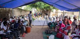 Eine große Gruppe von Menschen sitzt zusammen und eine Person in der Mitte spricht. 