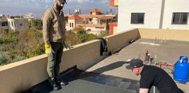 Anbringung von zwei Lagen Bitumenbahnen auf einem begehbaren Flachdach. Arbeiten erfolgen im Rahmen eines Trainingszwecks.