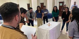 Das Bild zeigt junge Menschen, die gemeinsam mit einem an Schnüren fixiertem Stift etwas schreiben. 