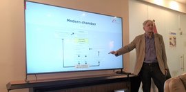 Das Bild zeigt einen Mann, der während eines bbw-Workshops vor einem großen Bildschirm steht und ein Flussdiagramm zu „Modern Chamber“ präsentiert. Der Sprecher erklärt die Vorteile einer modernen Kammer.