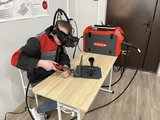Ein Auszubildender schweißt mit VR-Simulator, Headset und Fronius-Modul in Übungssituation.