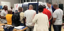 Die Teilnehmer der Delegationsreise schauen sich eine Maschine an. Eine Gruppe von Menschen steht vor einer Maschine und schaut sich die Maschine an. Eine Person erklärt die Maschine