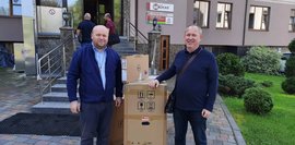 Zwei Männer stehen vor einem Gebäude und nehmen Kartons mit technischer Ausrüstung entgegen.