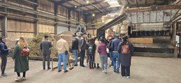 Gruppe bei Führung in Biogasanlage. Blick auf Grünschnitt-Anlage, Kran und Besucher.