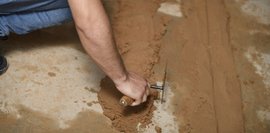 Ein Schüler verteilt Sand auf dem Boden mit einer Maurerkelle.