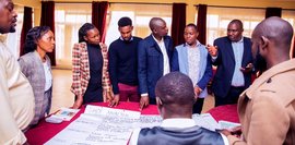 Eine Gruppe von Personen steht um einen Tisch und bespricht eine SWOT-Analyse, die auf großen Plakaten notiert ist.