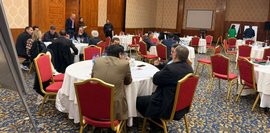 Gruppenarbeiten Eine Gruppe von Männern und Frauen sitzt an runden Tischen in einem Konferenzraum und diskutiert.