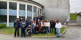 Eine Gruppe von etwa 20 Personen posiert vor einem Gebäude und einem grauen, schuppenartigen Turm.