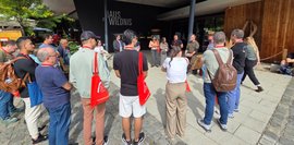 Eine Gruppe von Leuten steht vor dem "Haus zur Wildnis". Einige tragen rote Taschen.