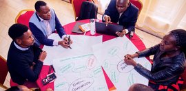 Sechs Personen sitzen um einen Tisch und arbeiten gemeinsam an Stakeholder-Diagrammen auf großem Papier.