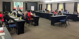 Qualitätszirkel in Südafrika im Hotel mit Teilnehmern von Colleges und Unternehmen, sowie staatlichen Institutionen Mehrere Menschen sitzen in Reihen in einem Seminarraum und eine Person steht vorne und präsentiert.