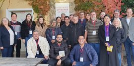 Eine Gruppe von etwa 20 Personen posiert vor einem Gebäude. Ein Schild wirbt für den Ersatz von Styropor. Herbstlaub umrahmt das Bild. Die Personen tragen unterschiedlich farbige Kleidung und Ausweise. Sie lächeln in die Kamera.