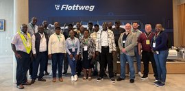 Eine Gruppe von 21 Personen steht vor einem Flottweg-Logo in einem hellen Raum. Viele tragen Namensschilder.