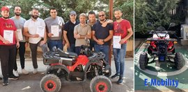 Eine Gruppe von Männern posiert stolz mit ihren Zertifikaten neben zwei roten Quads. Elektromobilität steht im Fokus. Fröhliche Stimmung.