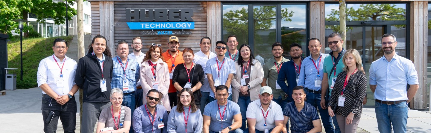 Eine Gruppe von 25 lächelnden Menschen steht vor dem Gebäude "Huber Technology".