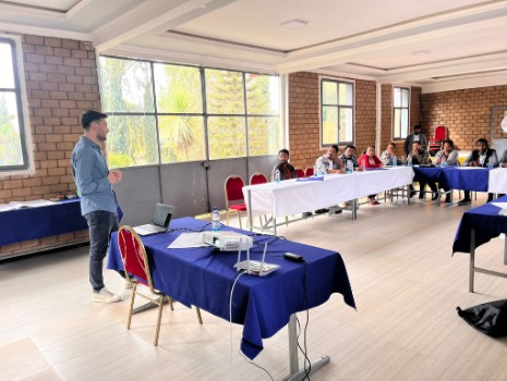 Das Bild zeigt einen bbw-Trainer, der in einem Raum mit Teilnehmern einen Workshop zur Arbeitssicherheit leitet. Der Trainer steht vor einem Tisch mit Laptop und Beamer. Die Teilnehmer sitzen an Tischen im Hintergrund.