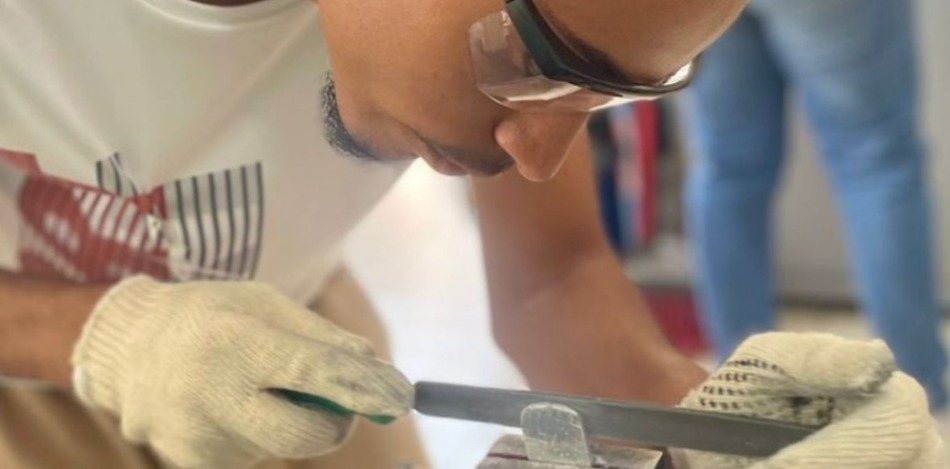 Das Bild zeigt einen Jugendlichen mit Schutzbrille, wie er an einer Erkennungsmarke feilt.