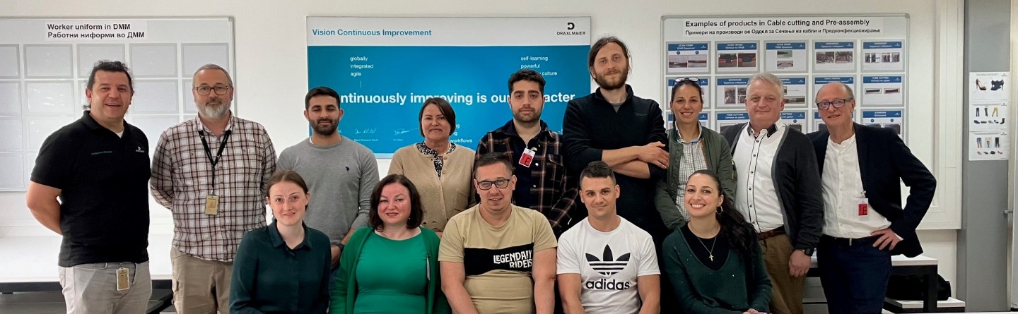 Die beteiligten Projektpartner sitzen in zwei Reihen in einem Seminarraum vor dem Dräxlmaier Logo. 