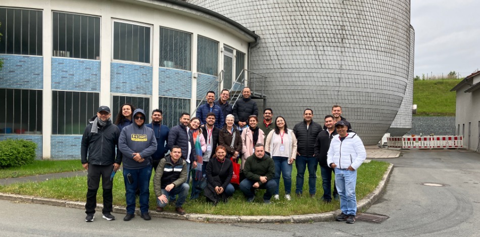 Eine Gruppe von etwa 20 Personen posiert vor einem Gebäude und einem grauen, schuppenartigen Turm.