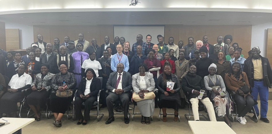 Eine große Gruppe von Menschen posiert für ein Foto in einem hell erleuchteten Raum. Die meisten sitzen oder stehen.