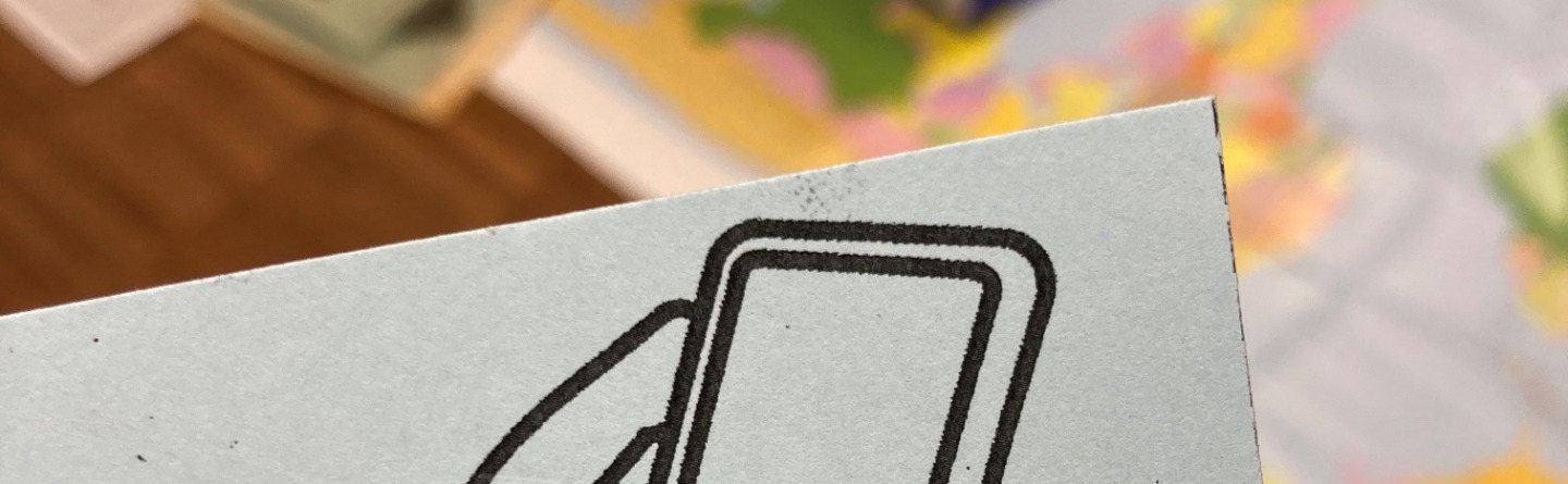 Nahaufnahme eines hellblauen Papiers mit einer schwarz-weiß Illustration: Zwei Hände halten ein Smartphone. Unscharfer Hintergrund mit Karte und Papier.