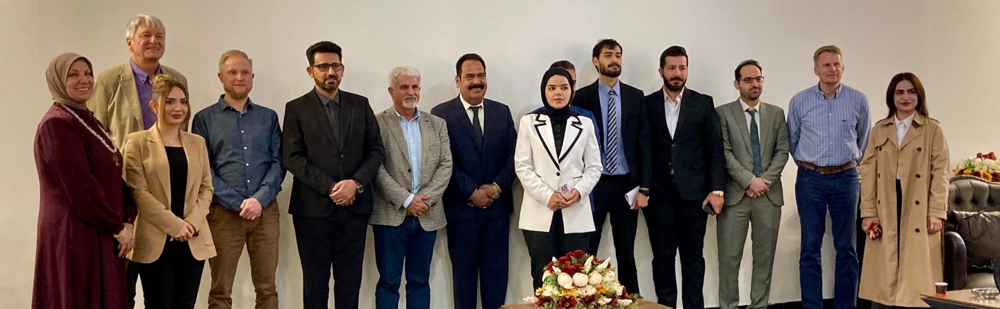 Gruppenfoto vom Feinplanungsworkshop der Kammer- und Verbandspartnerschaft Irak im März 2024. 14 Teilnehmer*innen stehen vor weißem Hintergrund. Blumenarrangement auf Tisch im Vordergrund.