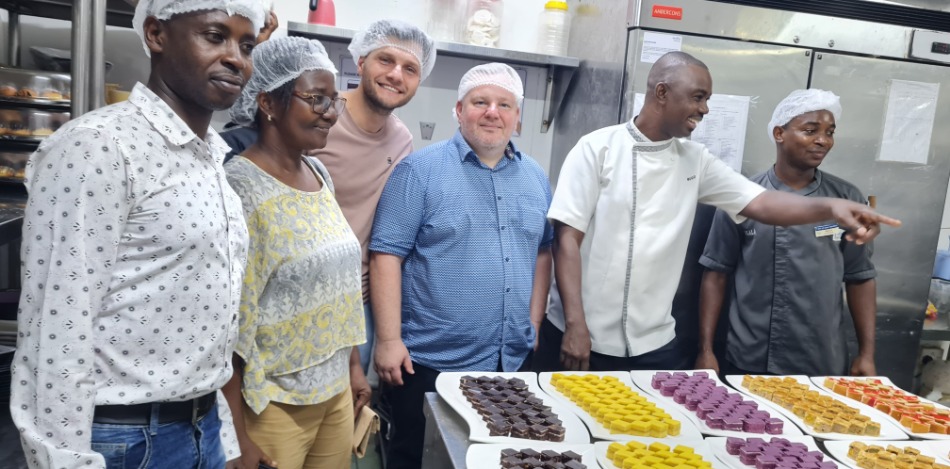 Hospitality-Trainer stehen in einer professionellen Trainingsküche hinter mehreren Tabletts mit sorgfältig angerichteten Gebäck- und Dessertprodukten. Das Bild zeigt praktische Ausbildungsergebnisse im Hospitality-Bereich.