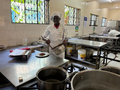 Eine Auszubildende im Hospitality-Bereich steht in weißer Kochkleidung in einer Trainingsküche des Kenya Coast National Polytechnic. Sie hält Küchenutensilien und nimmt an einer praktischen beruflichen Ausbildung teil.