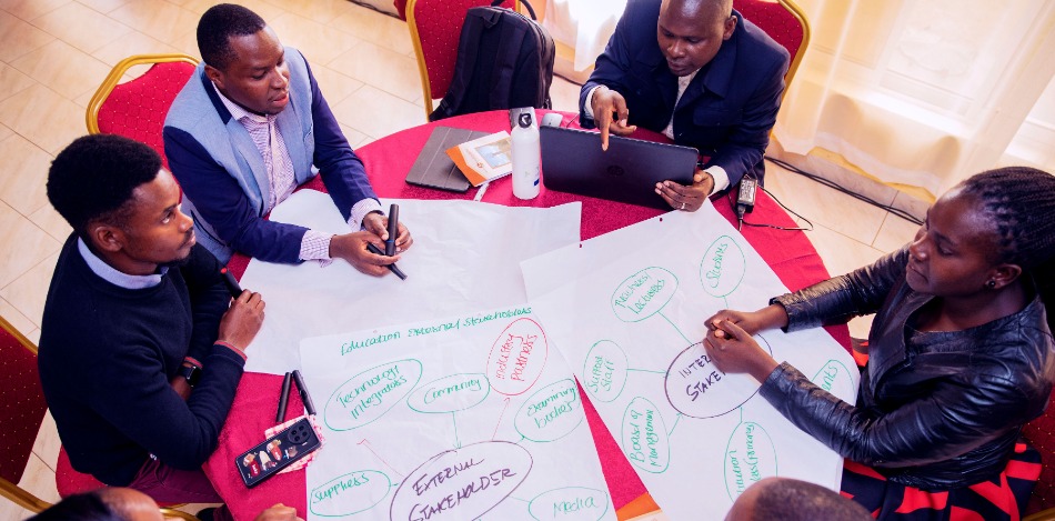 Sechs Personen sitzen um einen Tisch und arbeiten gemeinsam an Stakeholder-Diagrammen auf großem Papier.