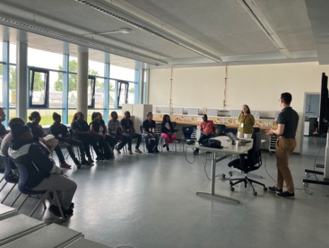 Eine Gruppe von Menschen sitzt in einem Seminarraum im Halbkreis und eine Person präsentiert im Stehen. 