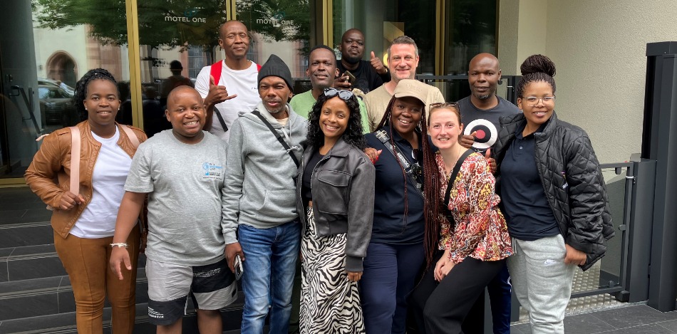 Eine Gruppe von Menschen steht vor dem Eingang eines Hotels in drei Reihen und macht ein fröhliches Gruppenfoto