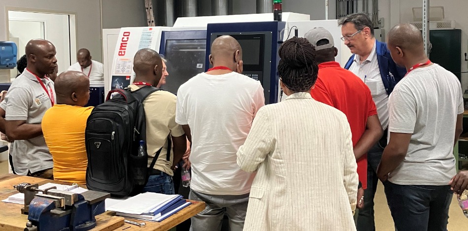 Eine Gruppe von Menschen steht vor einer Maschine und schaut sich die Maschine an. Eine Person erklärt die Maschine