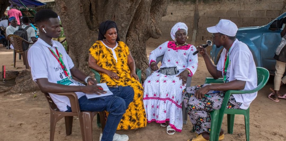 Vier Personen sitzen auf Stühlen vor einem Baum und diskutieren. 