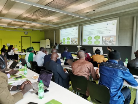 Mehrere Personen sitzen in Reihen in einem Semiarraum und eine Person präsentiert. 