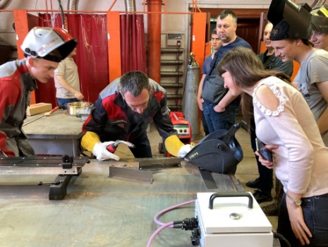 Ein erfahrener Ausbilder zeigt einer Gruppe Jugendlicher das Schweißen an einer Werkbank.
