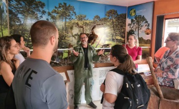 Gruppe hört einem Museumsführer zu. Hintergrund: Tier- und Pflanzenwandbilder.