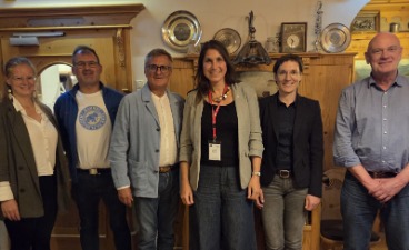 Sechs Personen stehen vor einem dekorierten Holzschrank und lächeln in die Kamera.