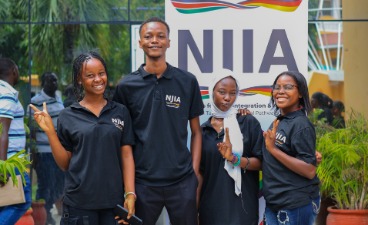 Bildung als Schlüssel Vier junge Menschen in schwarzen T-Shirts posieren fröhlich vor einem NJIA-Banner.