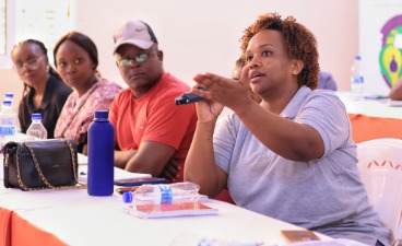 Workshop des Hotel- und Gastgewerbes Eine Frau spricht gestikulierend in ein Mikrofon, andere Personen sitzen am Tisch.
